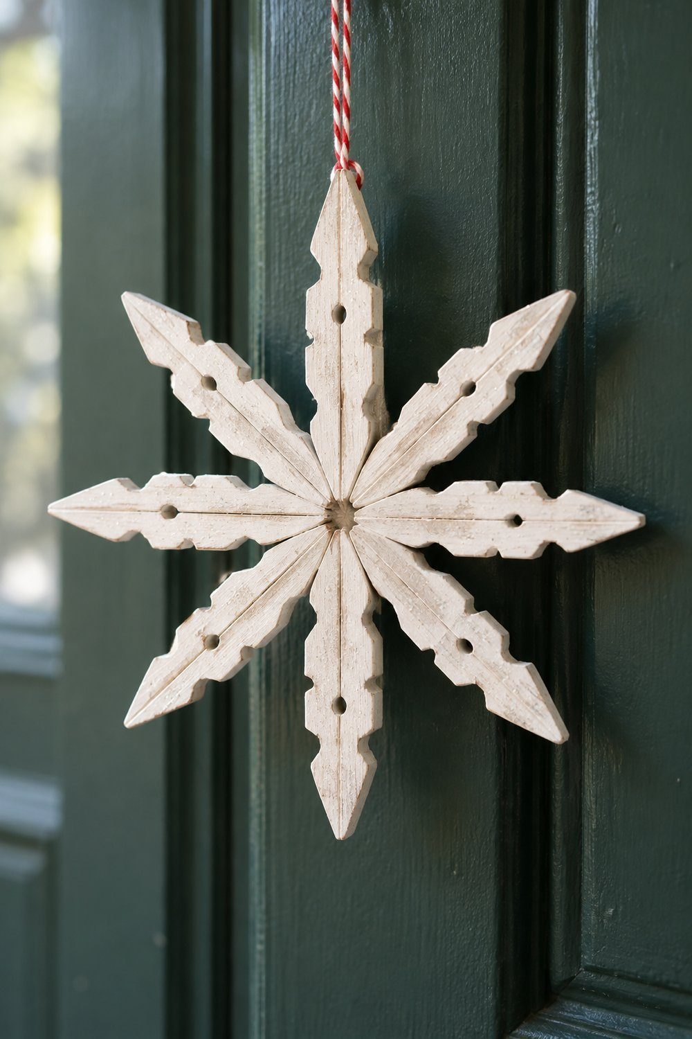 A pale white painted wooden clothespin snowflake with subtle glitter hangs from baker’s twine against