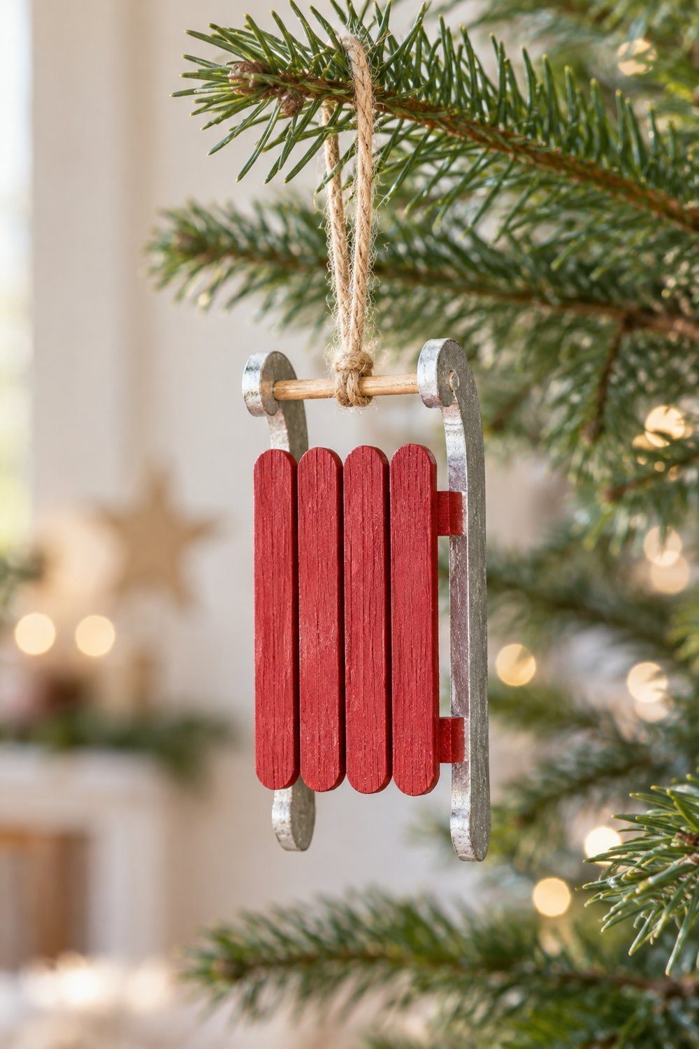 A tiny red craft stick sled with silver runners and a twine loop hangs on