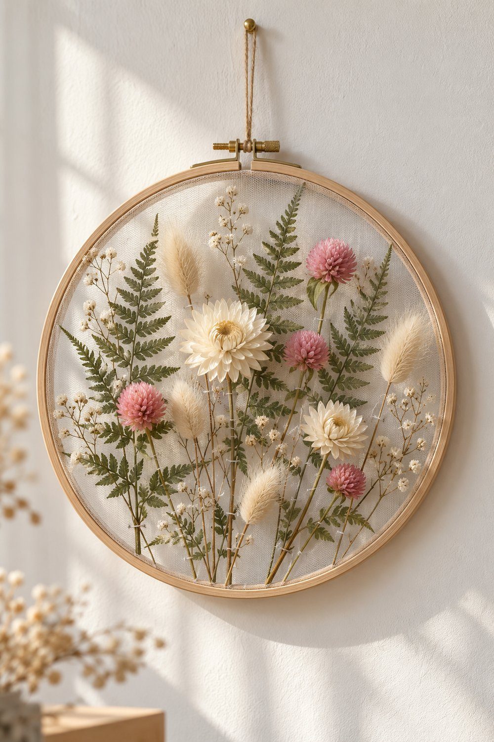 Wooden embroidery hoop displaying pressed ferns and dried flowers on transparent tulle